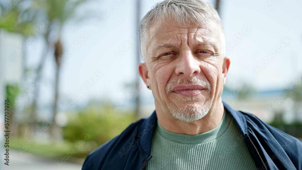 Middle age grey-haired man standing with serious expression at park Middle age grey-haired man standing with serious expression at park