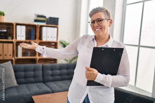 Middle age woman psychologist holding clipboard standing at pyschology center photo