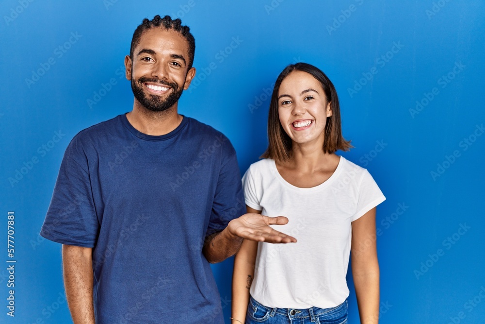 Young hispanic couple standing together smiling cheerful presenting and pointing with palm of hand looking at the camera. Young hispanic couple standing together smiling cheerful presenting and pointing with palm of hand looking at the camera.