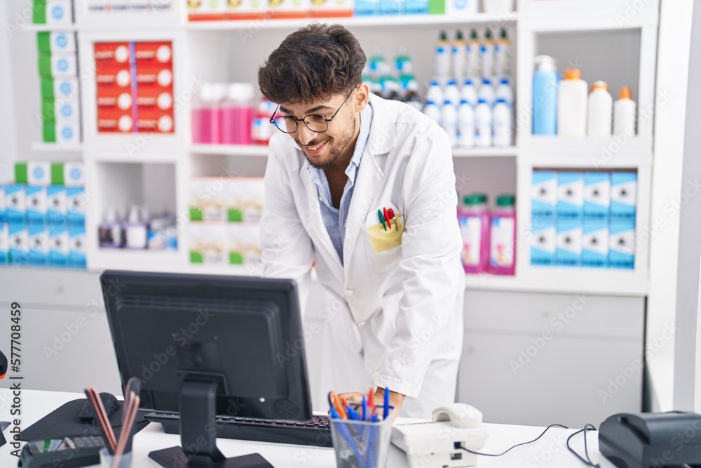 Young arab man pharmacist using computer working at pharmacy