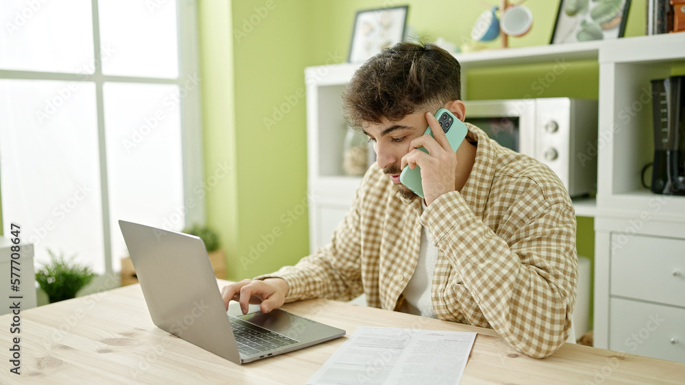 Young arab man using laptop talking on smartphone at home Young arab man using laptop talking on smartphone at home