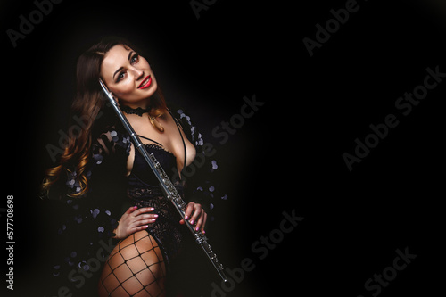 Smiling cover artist woman posing with flute at black isolated background, looking at camera. Chic lady flautist in black costume holding flute in hands. Orchestra music concept. Copy ad text space