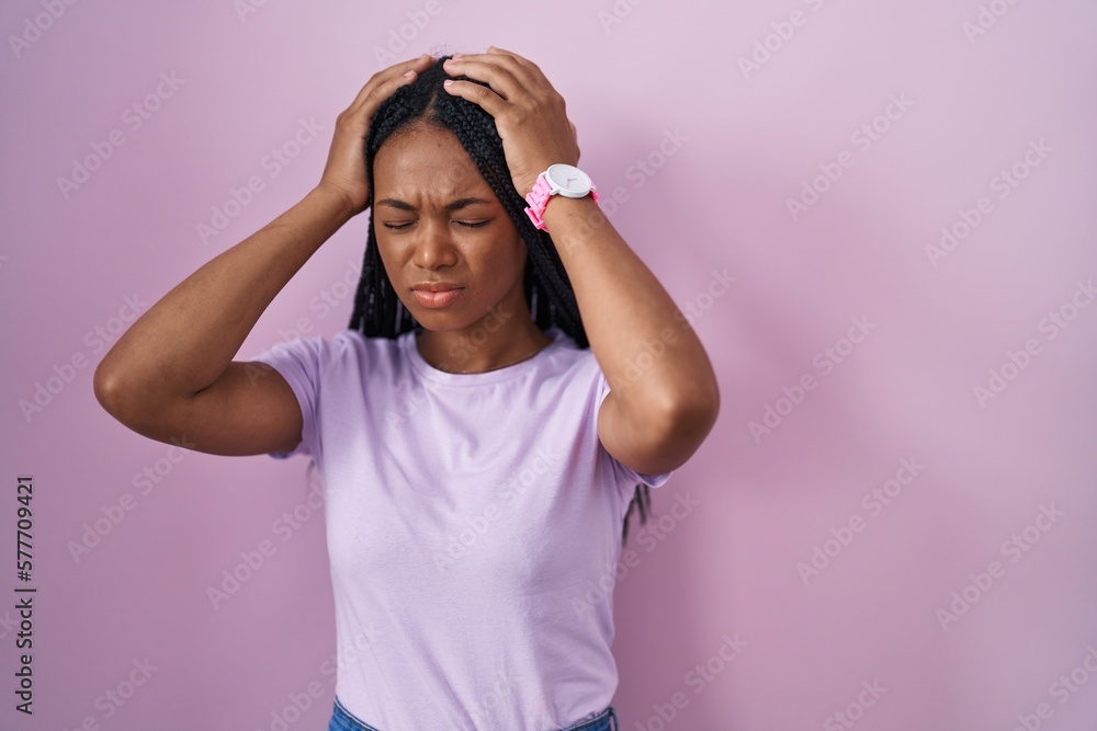 African american woman with braids standing over pink background suffering from headache desperate and stressed because pain and migraine. hands on head. African american woman with braids standing over pink background suffering from headache desperate and stressed because pain and migraine. hands on head.