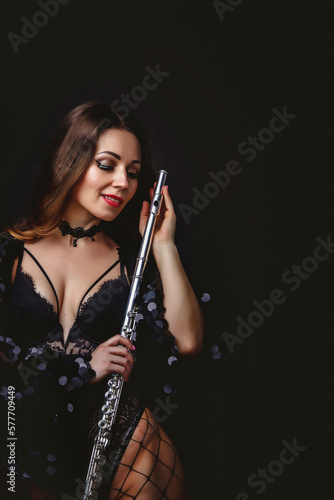 Smiling cover woman posing with flute at black isolated background, closed eyes. Happy chic lady flautist in black dress holding flute in hands. Orchestra music concept. Copy ad text space, banner