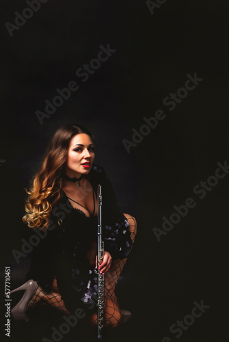 Graceful cover lady flautist posing with flute at black isolated background  looking at camera. Chic woman artist in black costume with flute. Orchestra music concept. Copy text space  ad banner