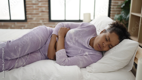 African american woman suffering for menstrual pain lying on bed at bedroom