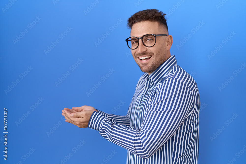 Fototapeta premium Hispanic man with beard wearing glasses pointing aside with hands open palms showing copy space, presenting advertisement smiling excited happy