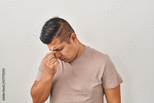 Hispanic young man standing over white background tired rubbing nose and eyes feeling fatigue and headache. stress and frustration concept. © Krakenimages.com