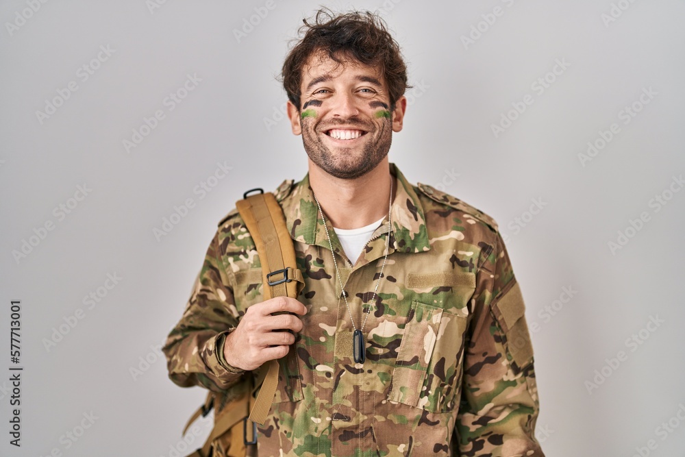 Hispanic young man wearing camouflage army uniform with a happy and cool smile on face. lucky person. Hispanic young man wearing camouflage army uniform with a happy and cool smile on face. lucky person.