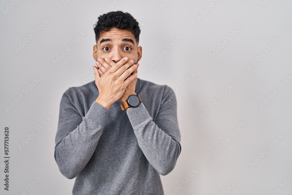 Hispanic man with beard standing over white background shocked covering mouth with hands for mistake. secret concept. Hispanic man with beard standing over white background shocked covering mouth with hands for mistake. secret concept.