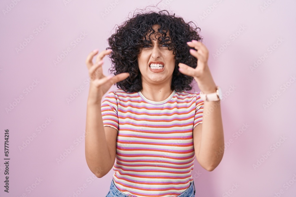 Young middle east woman standing over pink background shouting frustrated with rage, hands trying to strangle, yelling mad Young middle east woman standing over pink background shouting frustrated with rage, hands trying to strangle, yelling mad