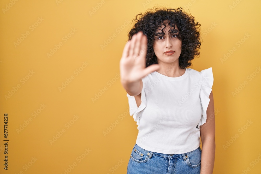 Young middle east woman standing over yellow background doing stop sing with palm of the hand. warning expression with negative and serious gesture on the face. Young middle east woman standing over yellow background doing stop sing with palm of the hand. warning expression with negative and serious gesture on the face.