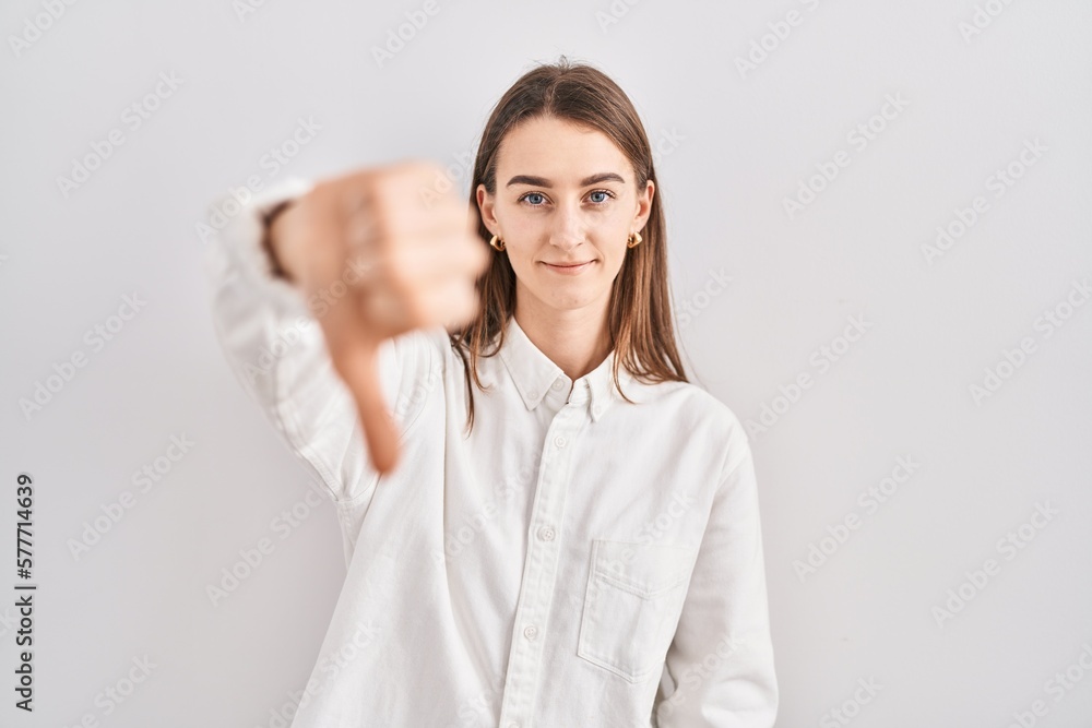 Young caucasian woman standing over isolated background looking unhappy and angry showing rejection and negative with thumbs down gesture. bad expression. Young caucasian woman standing over isolated background looking unhappy and angry showing rejection and negative with thumbs down gesture. bad expression.