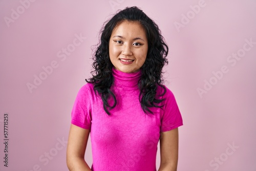 Young asian woman standing over pink background with hands together and crossed fingers smiling relaxed and cheerful. success and optimistic