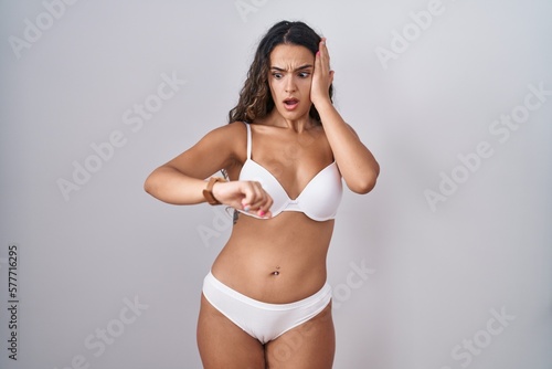 Young hispanic woman wearing white lingerie looking at the watch time worried, afraid of getting late