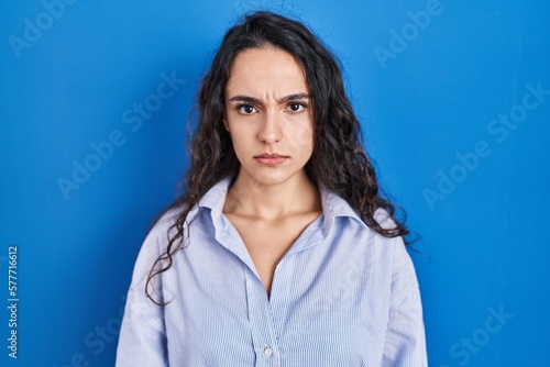 Young brunette woman standing over blue background skeptic and nervous, frowning upset because of problem. negative person.