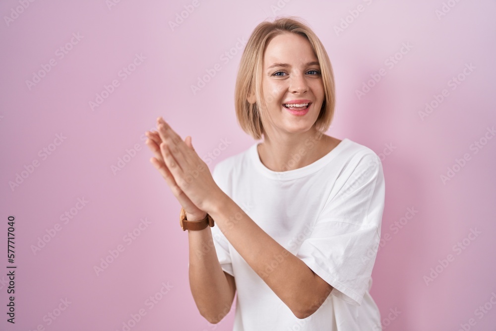 Young caucasian woman standing over pink background clapping and applauding happy and joyful, smiling proud hands together Young caucasian woman standing over pink background clapping and applauding happy and joyful, smiling proud hands together