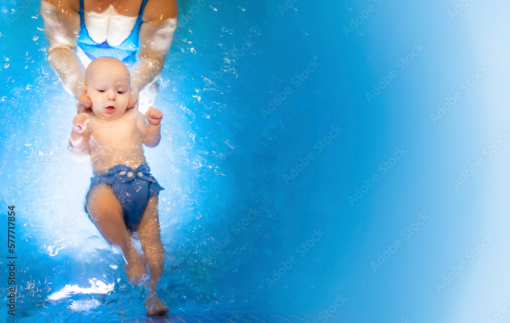 Adorable baby girl enjoying swimming in a pool with her mother early