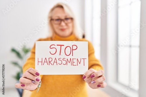 Middle age blonde woman business worker smiling confident holding stop harassement banner at office
