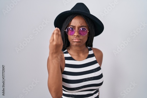 Young african american with braids wearing hat and sunglasses doing italian gesture with hand and fingers confident expression