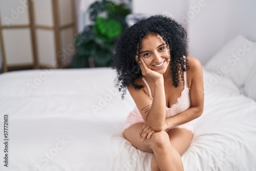 Young hispanic woman smiling confident sitting on bed at bedroom