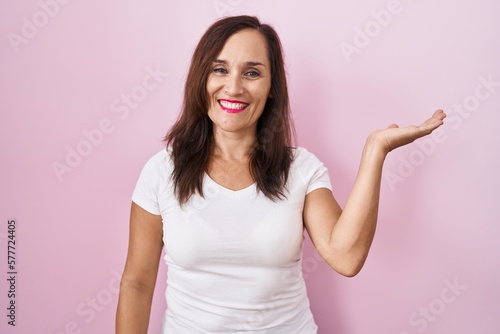 Wallpaper Mural Middle age brunette woman standing over pink background smiling cheerful presenting and pointing with palm of hand looking at the camera. Torontodigital.ca