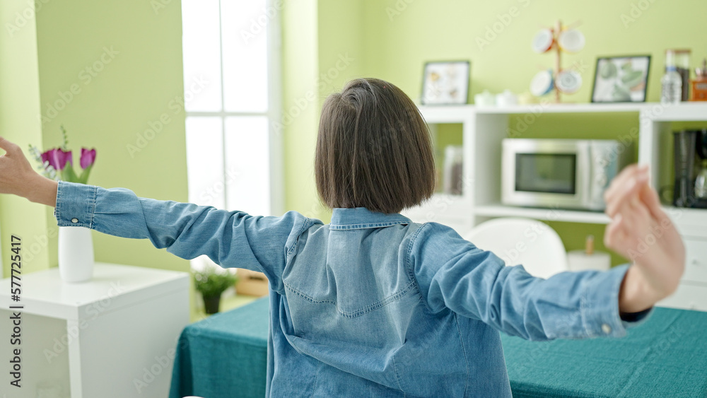 Young caucasian woman sitting on table stretching arms at home