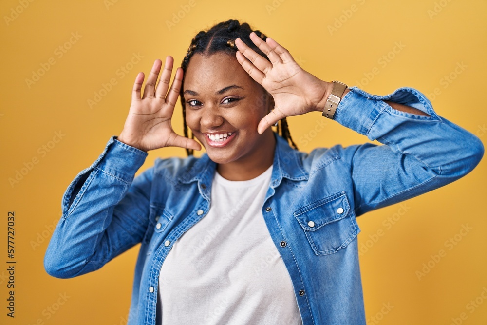 African american woman with braids standing over yellow background smiling cheerful playing peek a boo with hands showing face. surprised and exited African american woman with braids standing over yellow background smiling cheerful playing peek a boo with hands showing face. surprised and exited