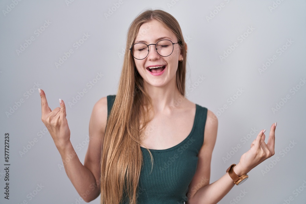Young caucasian woman standing over white background shouting with crazy expression doing rock symbol with hands up. music star. heavy music concept. Young caucasian woman standing over white background shouting with crazy expression doing rock symbol with hands up. music star. heavy music concept.