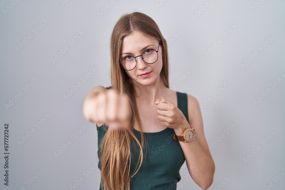 Φωτογραφία Young caucasian woman standing over white background punching fist to fight, agg