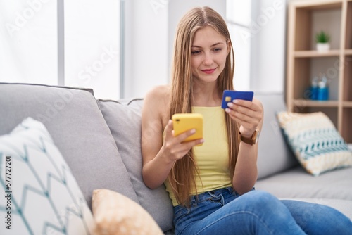 Young caucasian woman using smartphone and credit card sitting on sofa at home