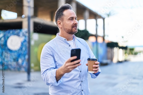 Young caucasian man using smartphone drinking coffee at street