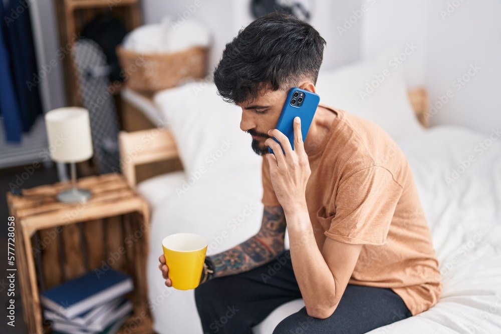 Young hispanic man talking on smartphone drinking coffee at bedroom Young hispanic man talking on smartphone drinking coffee at bedroom