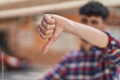 Young hispanic man doing negative gesture with thumb down at street