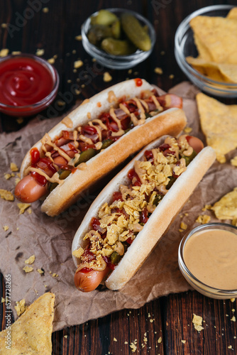 hot dogs with pickles, bacon, and nachos on a dark wooden background selective focus