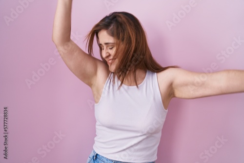 Brunette woman standing over pink background dancing happy and cheerful, smiling moving casual and confident listening to music