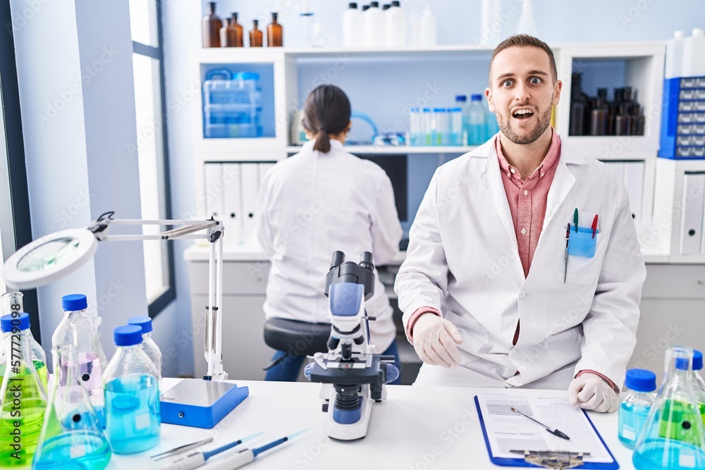 Young man working at scientist laboratory scared and amazed with open mouth for surprise, disbelief face Young man working at scientist laboratory scared and amazed with open mouth for surprise, disbelief face
