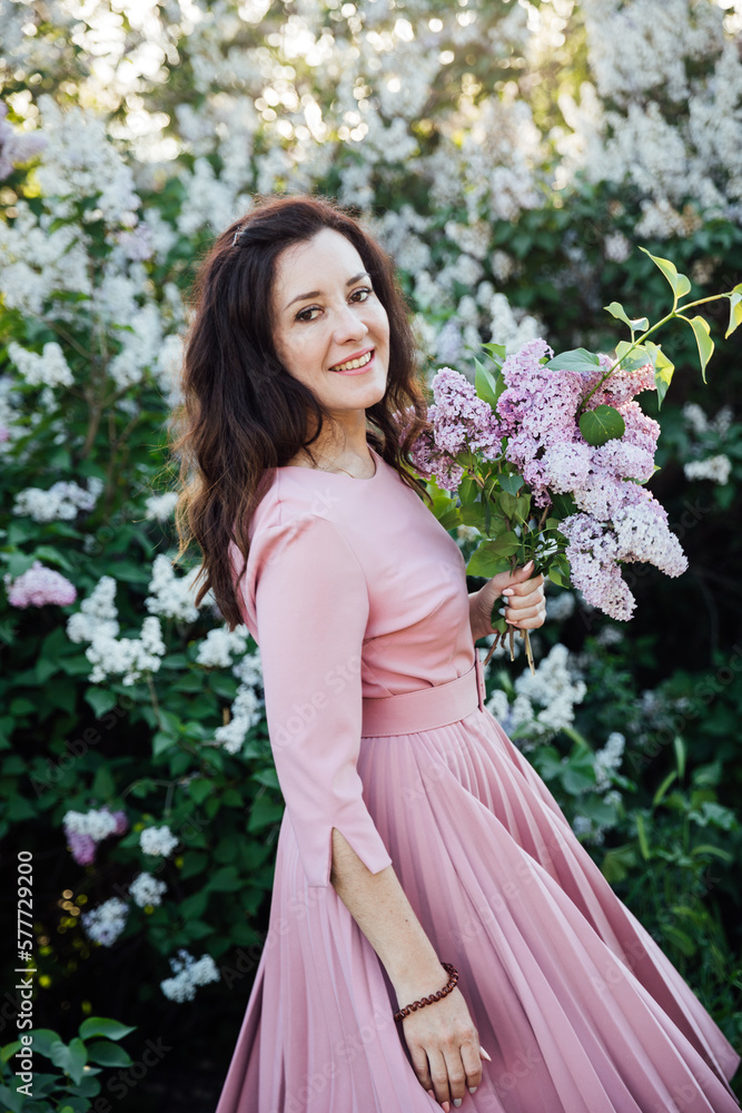 beautiful woman in a pink dress with a bouquet of lilacs on a background of flowers beautiful woman in a pink dress with a bouquet of lilacs on a background of flowers