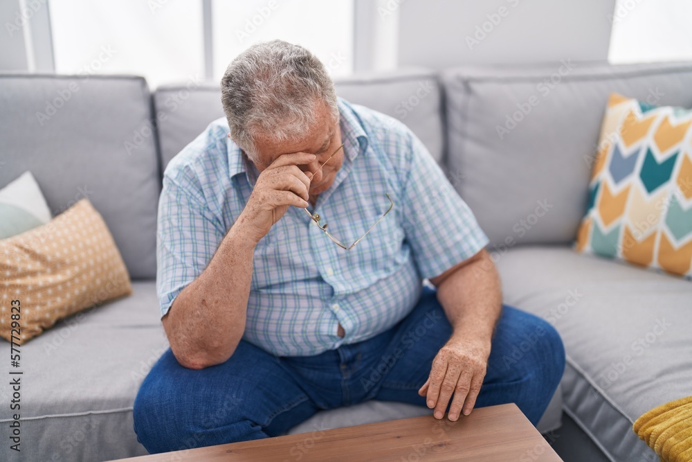 Middle age grey-haired man stressed sitting on sofa at home