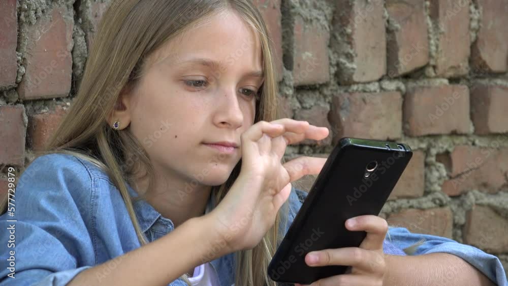Child Playing on Smartphone in Park, Kid Browsing Internet on Smart Phone, Blonde Teenager Girl Typing Messages Talking on Device Child Playing on Smartphone in Park, Kid Browsing Internet on Smart Phone, Blonde Teenager Girl Typing Messages Talking on Device