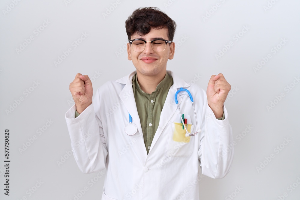 Young non binary man wearing doctor uniform and stethoscope excited for success with arms raised and eyes closed celebrating victory smiling. winner concept. Young non binary man wearing doctor uniform and stethoscope excited for success with arms raised and eyes closed celebrating victory smiling. winner concept.