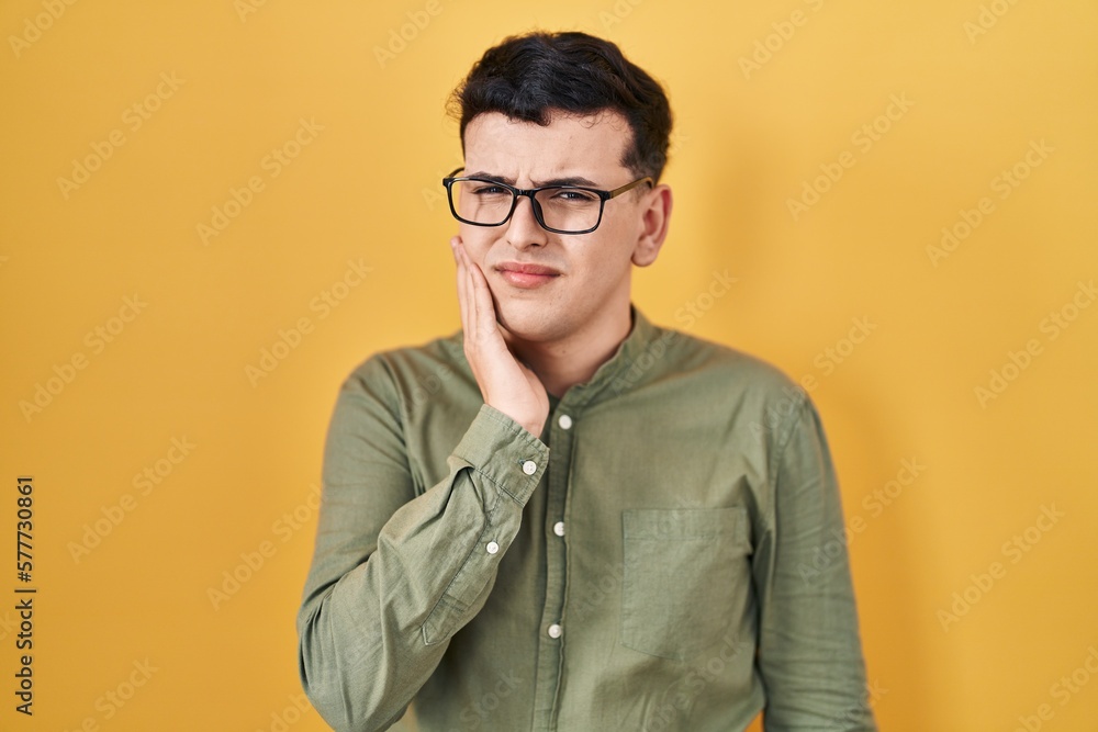Obraz premium Non binary person standing over yellow background touching mouth with hand with painful expression because of toothache or dental illness on teeth. dentist