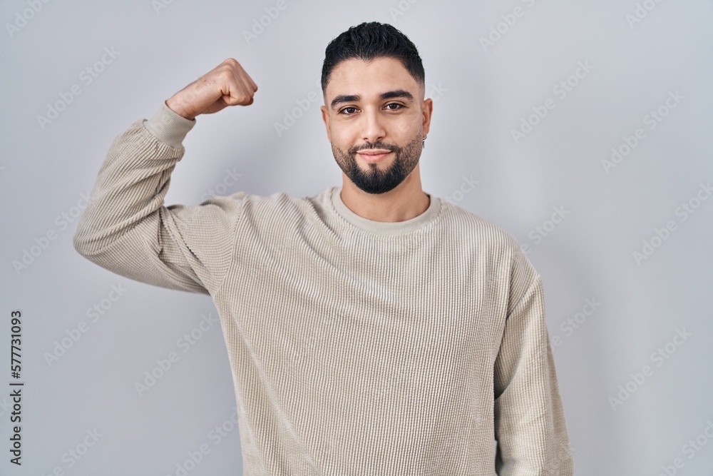 Young handsome man standing over isolated background strong person showing arm muscle, confident and proud of power Young handsome man standing over isolated background strong person showing arm muscle, confident and proud of power