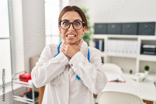 Young brunette doctor woman wearing stethoscope at the clinic shouting and suffocate because painful strangle. health problem. asphyxiate and suicide concept.