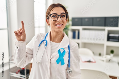 Young brunette doctor woman wearing stethoscope at the clinic showing and pointing up with finger number one while smiling confident and happy.