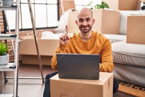 Young bald man with beard moving to a new house using laptop surprised with an idea or question pointing finger with happy face, number one