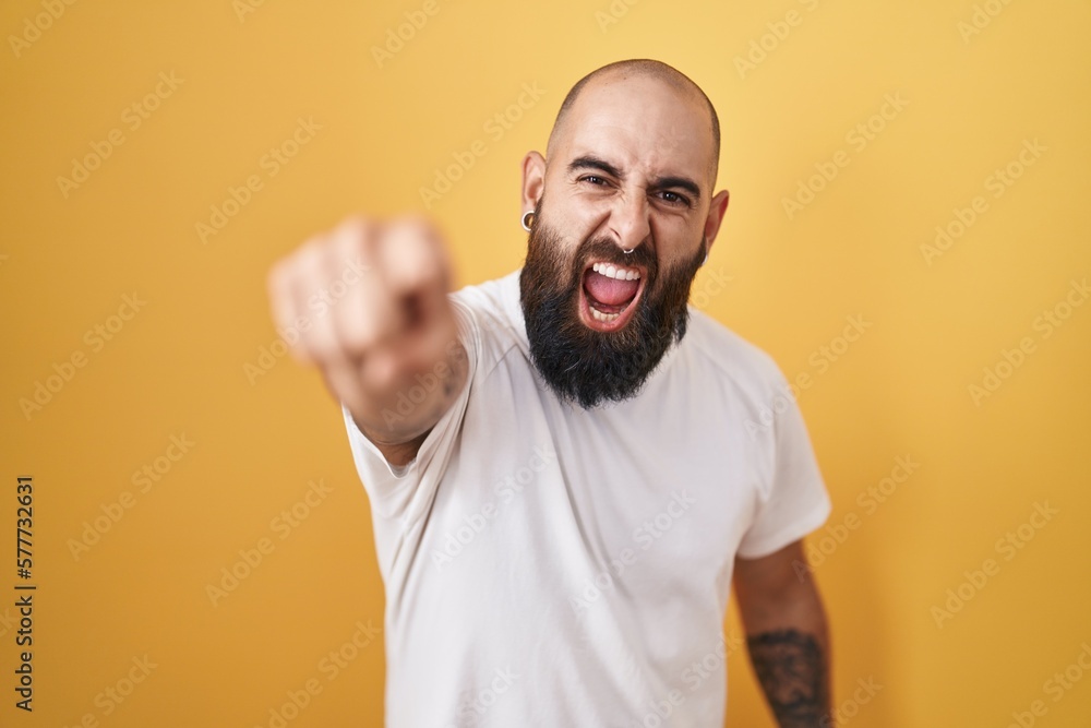Young hispanic man with beard and tattoos standing over yellow background pointing displeased and frustrated to the camera, angry and furious with you Young hispanic man with beard and tattoos standing over yellow background pointing displeased and frustrated to the camera, angry and furious with you