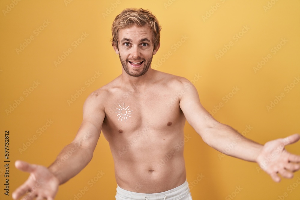 Caucasian man standing shirtless wearing sun screen looking at the camera smiling with open arms for hug. cheerful expression embracing happiness.