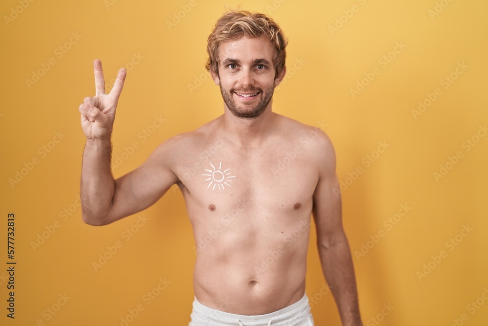 Caucasian man standing shirtless wearing sun screen showing and pointing up with fingers number two while smiling confident and happy.