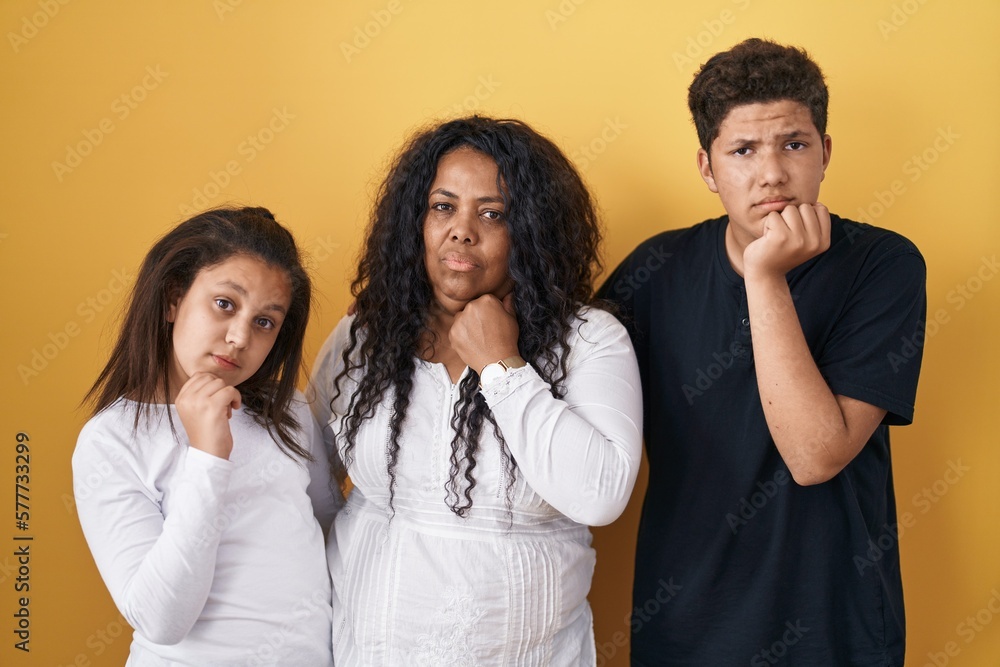Family of mother, daughter and son standing over yellow background with hand on chin thinking about question, pensive expression. smiling with thoughtful face. doubt concept. Family of mother, daughter and son standing over yellow background with hand on chin thinking about question, pensive expression. smiling with thoughtful face. doubt concept.